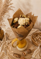 Bouquet Beige de Lune en cire végétale parfumée Odissa – roses ivoire et fleurs chocolat dans emballage kraft, posé sur vase moutarde