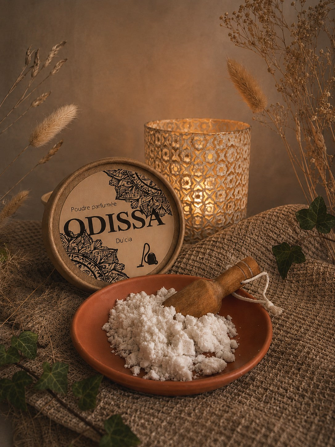 Poudre parfumée artisanale Odissa Dulcia dans une coupelle en terre cuite avec pelle en bois, boîte ronde à motifs mandala, bougeoir doré et lierre vert sur fond de graminées séchées et miroir doré