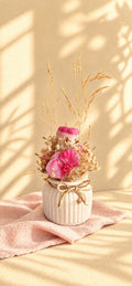 Composition florale en cire végétale rose avec orchidée fuchsia, roses et fleurs séchées dans un vase ivoire strié