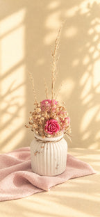 Composition florale en cire végétale avec orchidée rose, roses et graminées dorées dans un vase ivoire