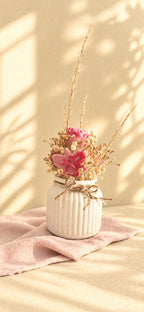 Composition florale en cire végétale avec rose fuchsia, orchidée rose et fleurs séchées dans un vase ivoire