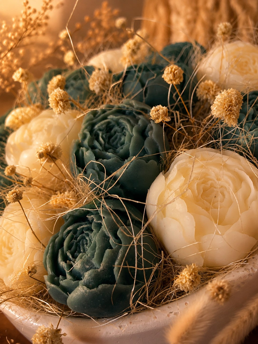Gros plan sur les roses en cire végétale Odissa – pétales sculptés bleu-vert et ivoire avec fleurs séchées dorées