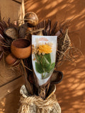 Rose jaune en cire végétale posée dans un bouquet de matières naturelles