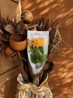 Rose jaune en cire végétale posée dans un bouquet de matières naturelles