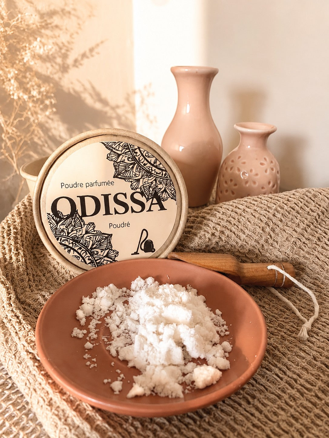 Poudre parfumée artisanale Odissa Poudré présentée dans une coupelle en terre cuite au premier plan, boîte ronde avec motifs mandala et vases roses sur fond beige chaud