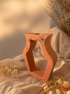 Vase ajouré en résine minérale terracotta Odissa – structure ajourée aux reflets dorés, entouré de fleurs séchées sur tissu crème