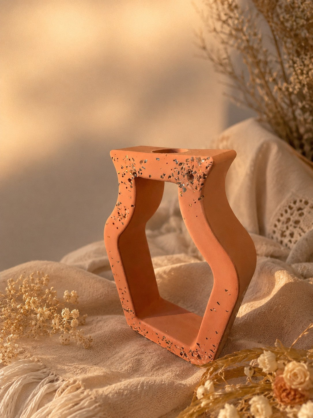 Vase ajouré en résine minérale terracotta Odissa – structure ajourée aux reflets dorés, entouré de fleurs séchées sur tissu crème