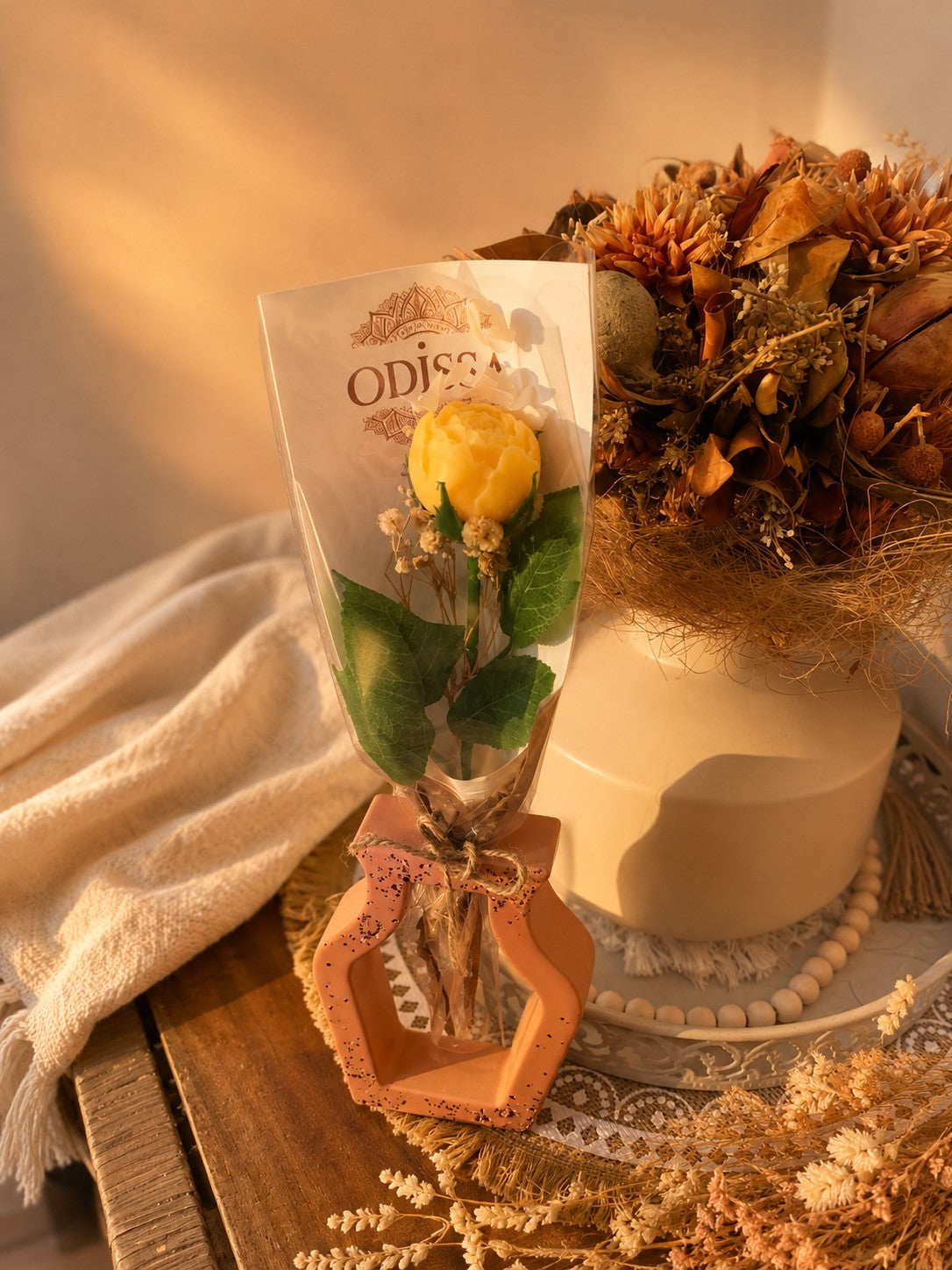 Vase ajouré en résine minérale terracotta Odissa avec rose en cire végétale jaune, présenté sur plateau blanc décoré de fleurs séchées